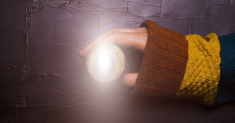 Närbild på en hand som håller ett värmeljus som står på en mörk yta.