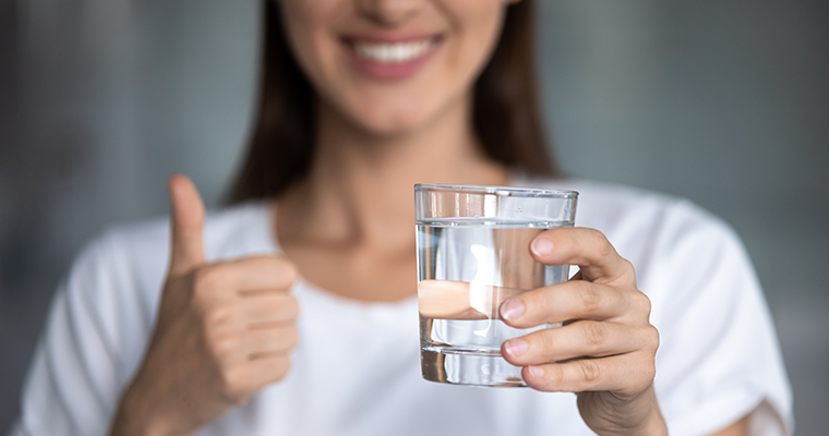 Oidentifierbar glad kvinna håller upp ett glas dricksvatten och gör tummen upp.