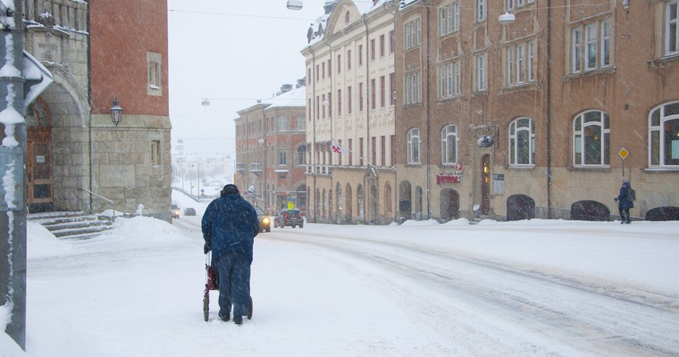en person med rollator går längs en stadsgata i snöfall