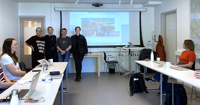 Mötesdeltagare runt ett hästskoformat bord, tittar mot fyra personer vid en whiteboard. 