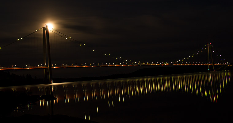 Högakustenbron speglar sig Ångermanälven på kvällen.