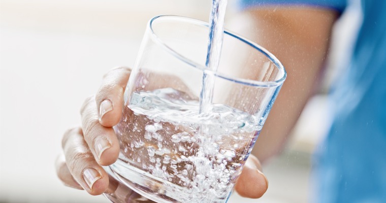 en hand håller ett vattenglas som fylls på under en vattenkran 