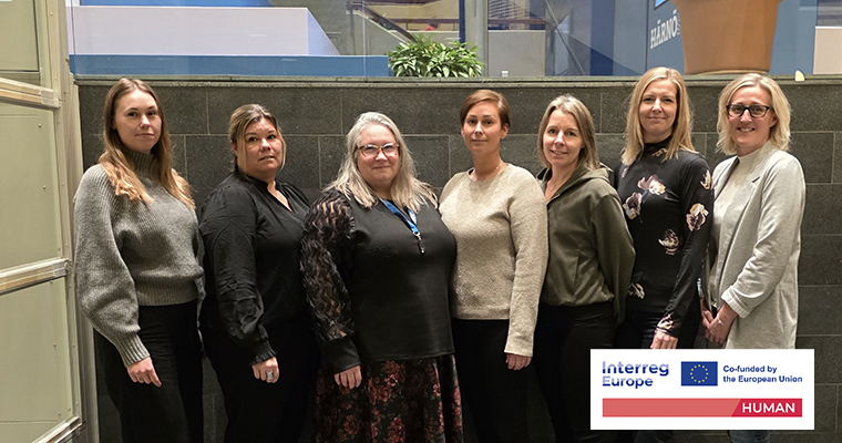 Gruppbild med sju kvinnor som är uppställda för fotografering inomhus.