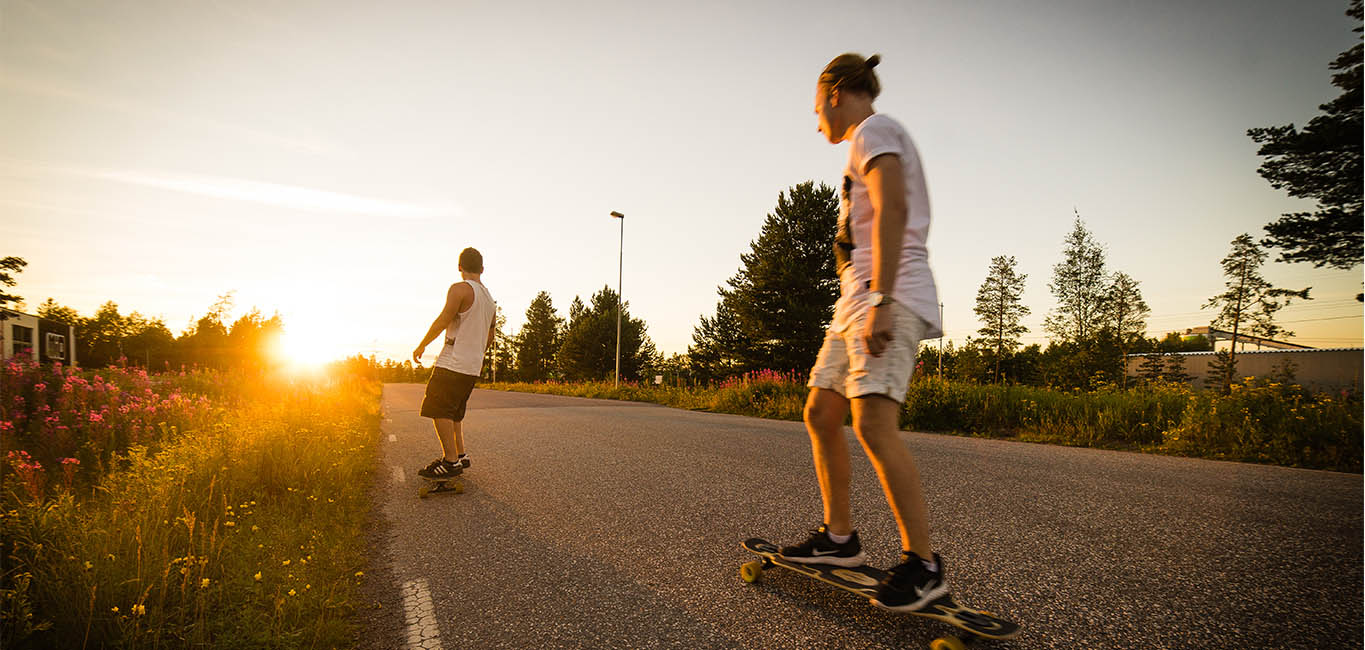 två personer åker skateboard på en asfalterad landsväg mot en solnedgång