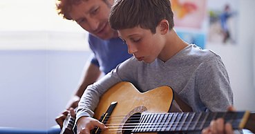 Lärare och elev tränar på att spela gitarr tillsammans.