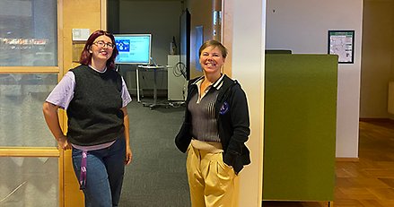 Två glada kvinnor som står vid en öppen dörr in till en möteslokal.