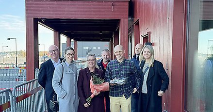 åtta personer framför en röd byggnad