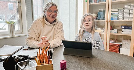 en kvinna och en skolflicka sitter vid ett bord med en läsplatta framför sig