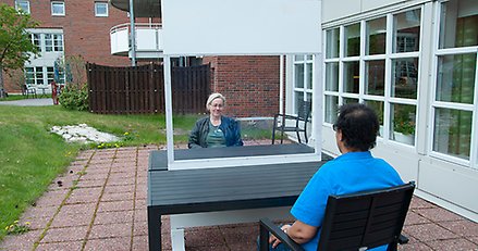 två personer som sitter på varsin sida av en skärm av plexiglas