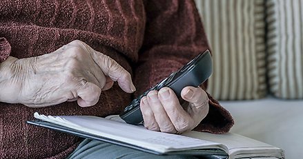 Äldre person med mobiltelefon i handen.