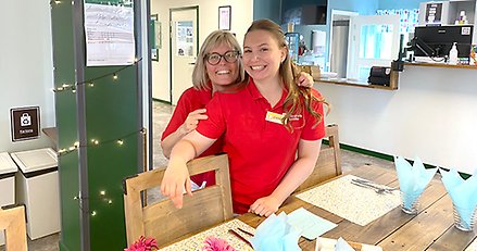 Två glada kvinnor dukar i ett fik. 