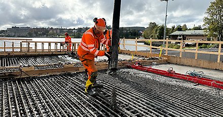 en person med orange arbetskläder håller en stor slang över en stor yta med armeringsjärn