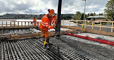 en person med orange arbetskläder håller en stor slang över en stor yta med armeringsjärn