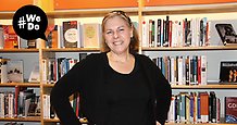 Porträttbild på bibliotekschef Susanne Hägglund som står framför några bokhyllor. I höga hörnet ett #WeDo-märke