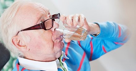 äldre man dricker ett glas med vatten