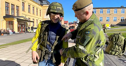 En man i grön uniform hjälper en gymnasieelev att ta på sig militär utrustning.
