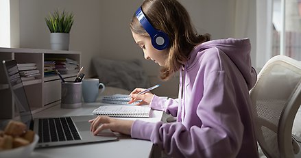 Ung tjej som sitter vid en dator och gör anteckningar i ett block.