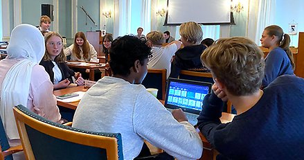 Högstadieelever diskuterar och planerar i en stor möteslokal.