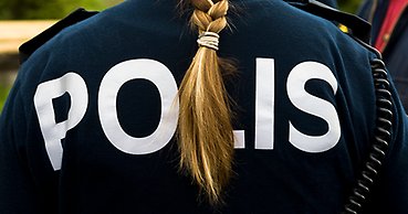 Ryggtavla på en oidentifierbar kvinnlig polis med fläta. Texten POLIS syns på ryggen.