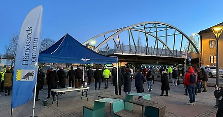 stålbro fraktas på trailer i bebyggelse, människor står bredvid och tittar på