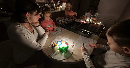 Familj sitter och pysslar runt ett bord upplyst av stearinljus.