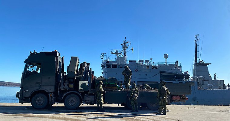 Soldater i uniform förbereder sig för att lasta av materiel från en lastbil till ett stort fartyg.