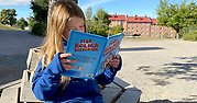 Flicka sitter på skolgården och läser en bok.
