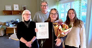 Fyra leende personer, en man och tre kvinnor. Kvinnan i mitten visar upp ett diplom och en blombukett.