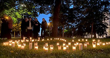 En stor mängd gravljus på marken i en mörk park. I bakgrunden fyra kvinnor.