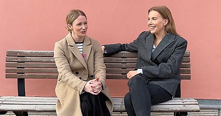 två unga kvinnor sitter på en bänk vid en vägg