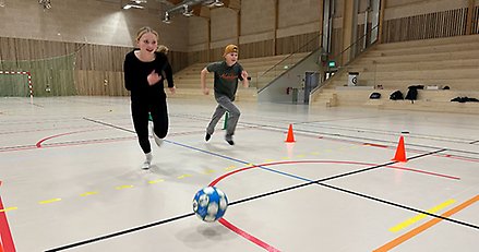 två barn springer med en fotboll i en idrottshall