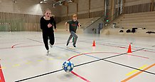 två barn springer med en fotboll i en idrottshall