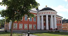 Exteriör bild på rådhuset i Härnösand. röd orange stenbyggnad med vita pelare.