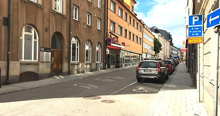 en stadsgata med parkerade bilar längs ena sidan