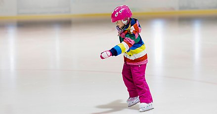 ett barn med hjälm åker skridskor i en ishall