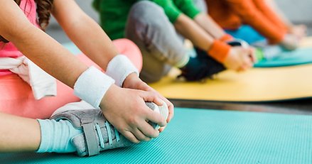 närbild på armar och ben på några personer som sitter och stretchar i en gymnastiksal