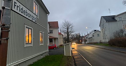 vy över en gata med en gatunamnsskylt i förgrunden och en bil med ljusen tända långt bort