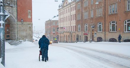 en person med rollator går längs en stadsgata i snöfall