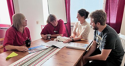 Fyra vårdanställda sitter samlade runt ett bord och tittar tillsammans i ett utbildningsmaterial.