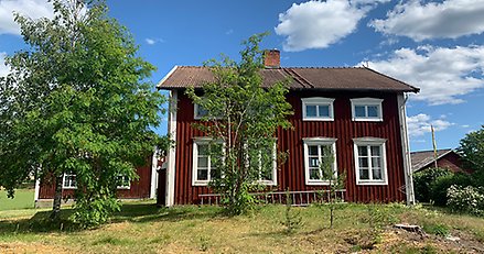 ett äldre rött trähus på landsbygden med blå himmel i bakgrunden