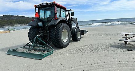 en traktor med en harv kör på en sandstrand vid havet