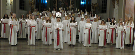 lucia, tärnor och stjärngossar står glest längst fram i kyrkan