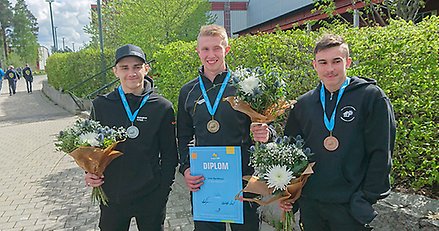 Tre ungdomar står bredvid varandra med medaljer om halsen och blombuketter i händerna.