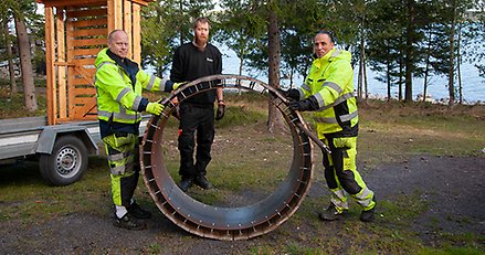 trepersoner står med en stor metallring mellan sig