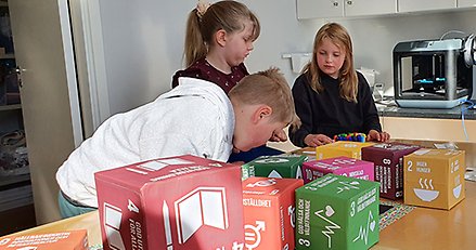 Tre barn sitter vid ett bord med kuber som föreställer de globala målen.