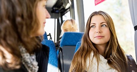 en ung kvinna sitter i en buss. I förgrunden syns en annan person suddigt i profil.