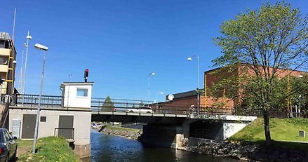 en mindre bro över ett sund. I bakgrunden en stor röd byggnad