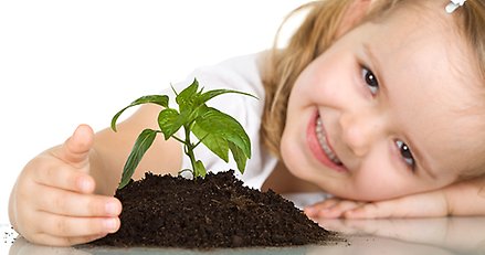 Liten glad flicka håller sin hand kring en liten jordhög med en planta