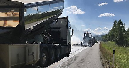 två stora fordon som jobbar med beläggningen på en väg på landsbygden