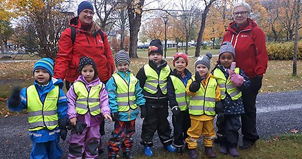 en gruppbarn med reflexvästar och två vuxna i en park